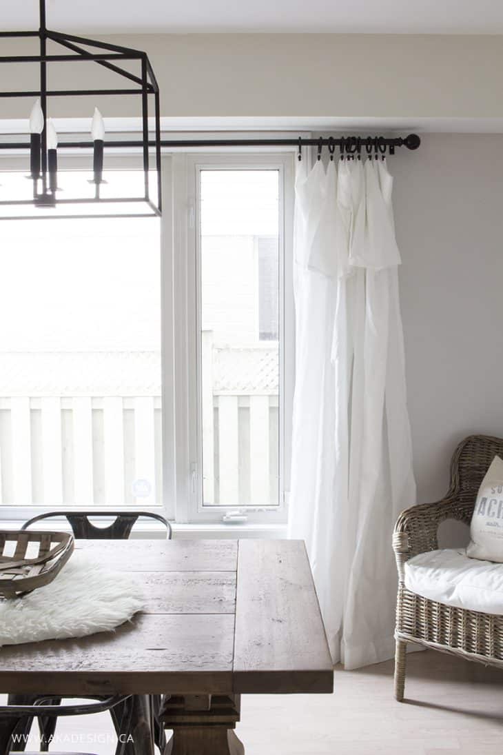 white dining room wood table whicker chair in corner white sheer curtains on window